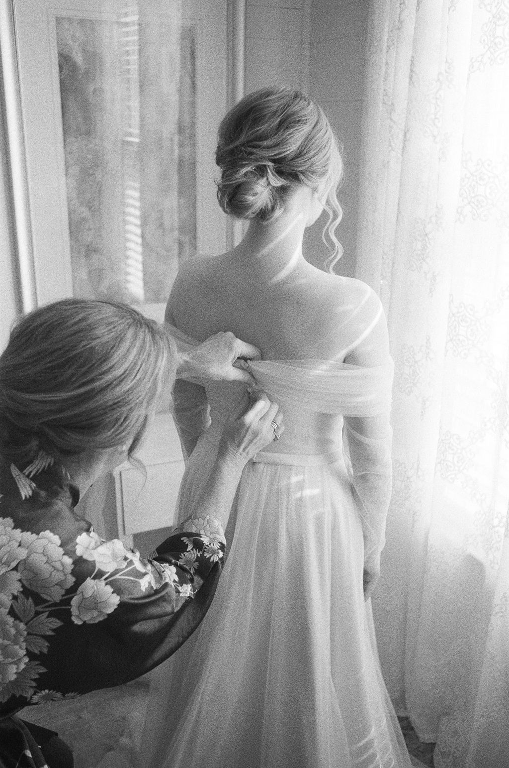 Black and white film of mom zipping bride's dress