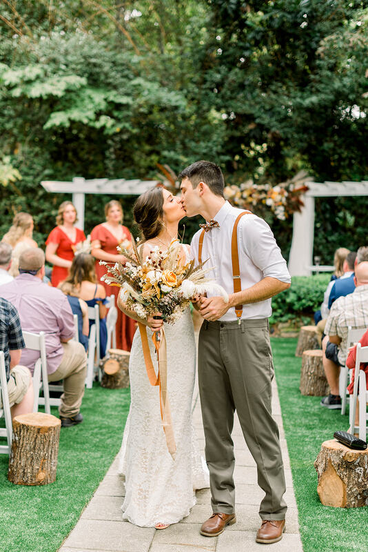 boho fall bride and groom kissing in outdoor ceremony aisle