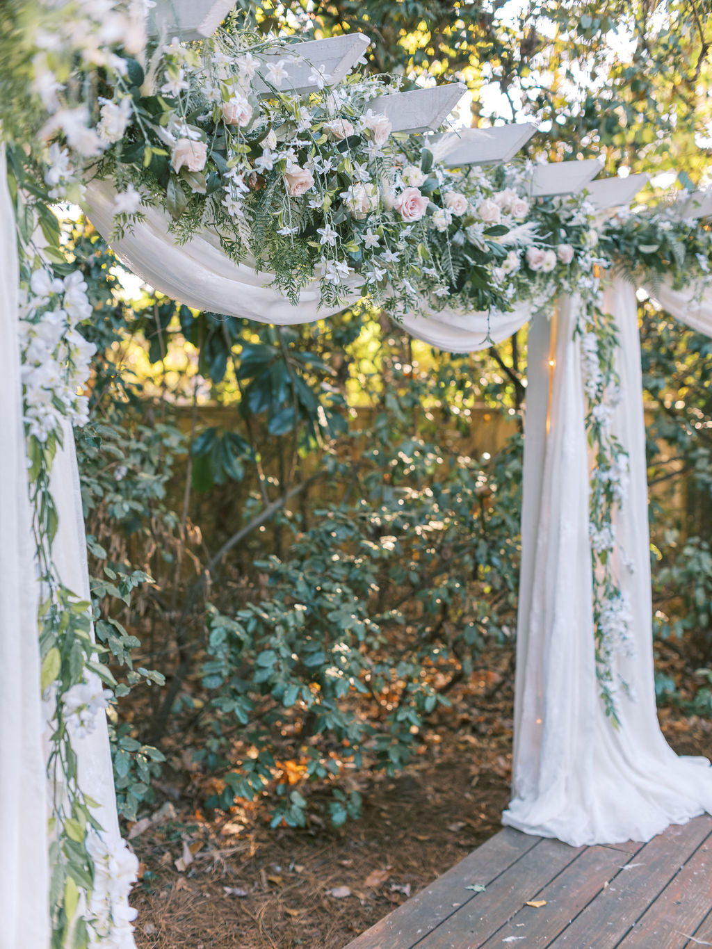garden wedding altar with white drapes, greenery, and white and blush flowers