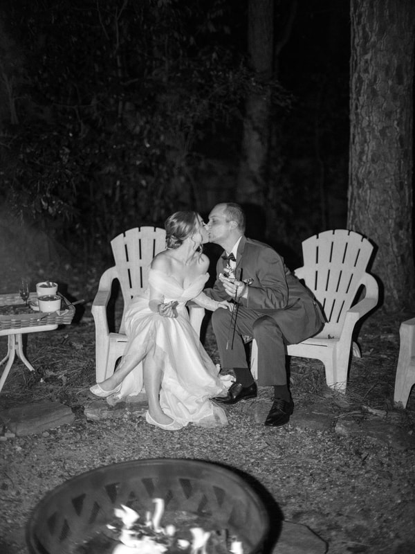 black and white photo of bride and groom kissing at firepit