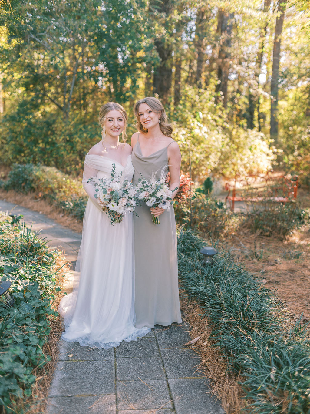 bride standing in garden path with bridesmaid in sage green dress