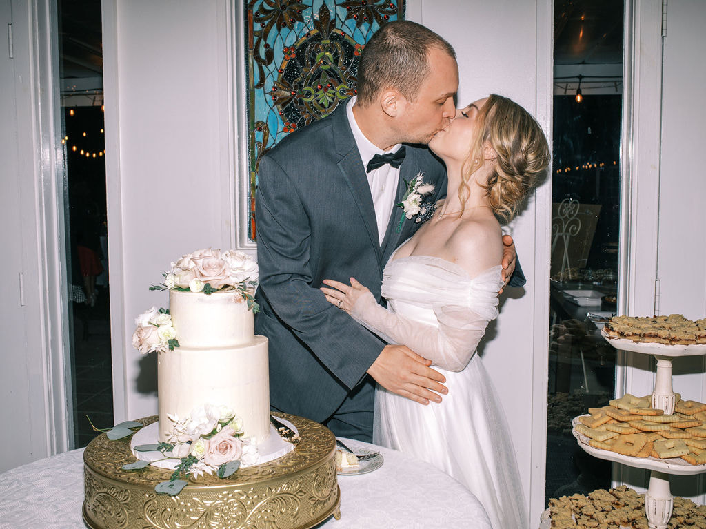 film photo of bride and groom kissing by cake display