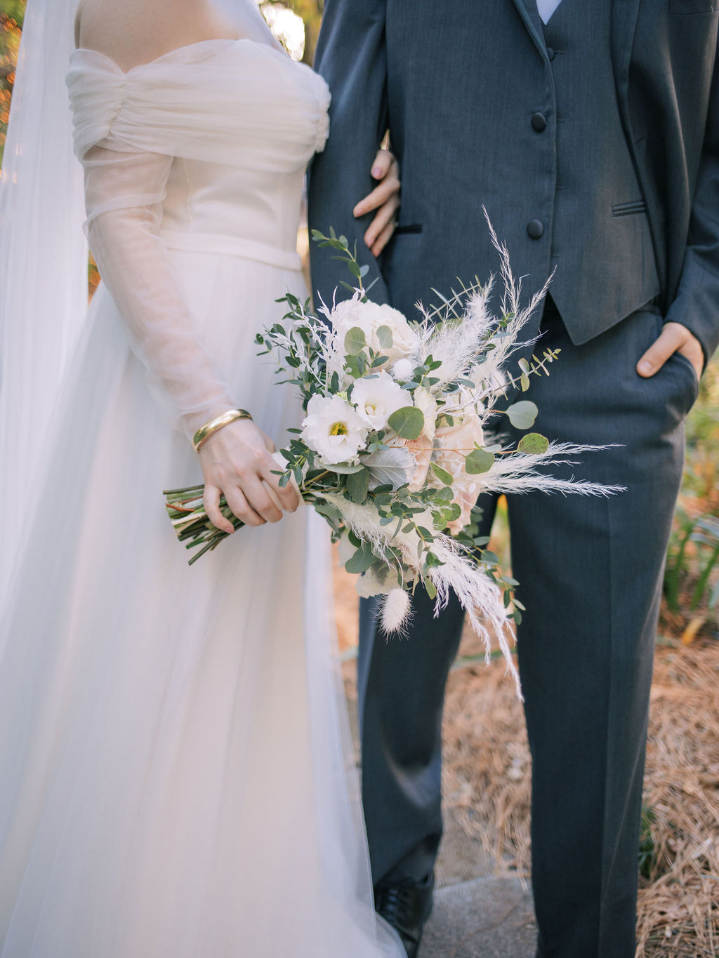 detail photo of bride and groom posing together, showing of bride's bouquet and gold bracelet
