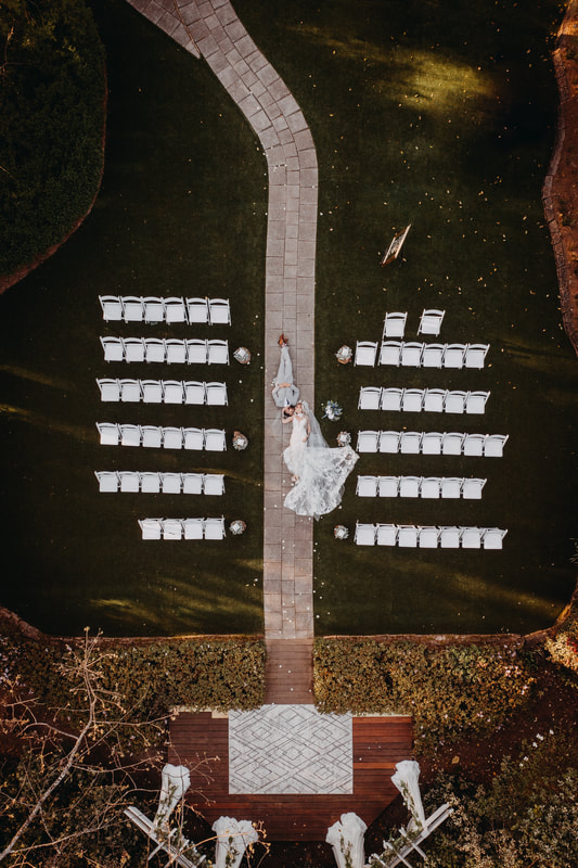 drone shot of bride and groom laying in outdoor garden ceremony aisle