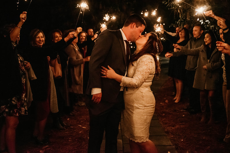 bride in knee-length white dress kissing groom during sparkler grand exit