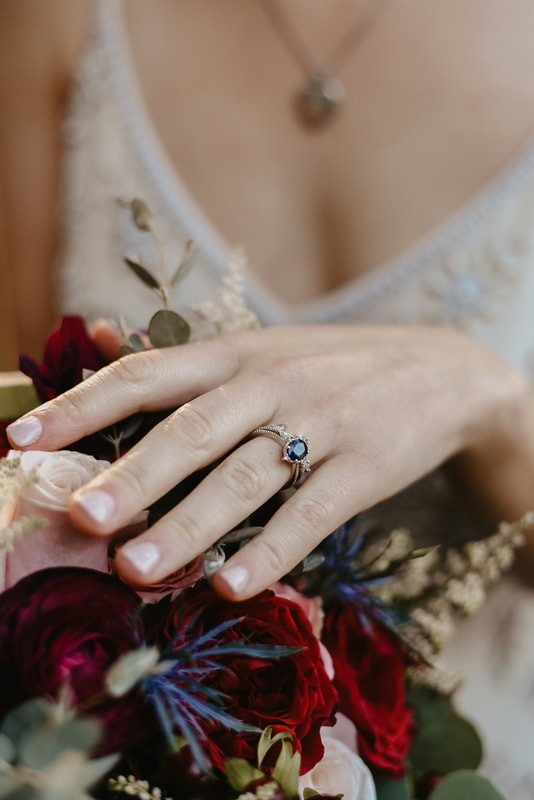 bride's jewel engagement ring with hand on bouquet