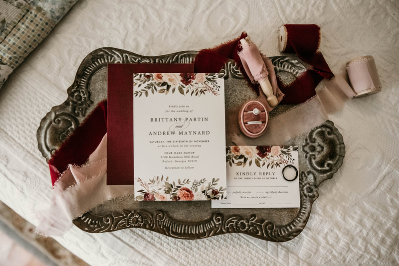 detail shot of wedding invitation and rings with burgundy and blush accent colors
