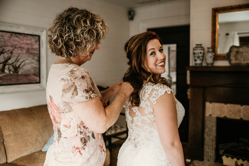 mother-of-the-groom buttoning up bride's lace dress