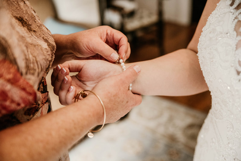 groom's mother helping bride put on pearl bracelet while getting ready for wedding ceremony