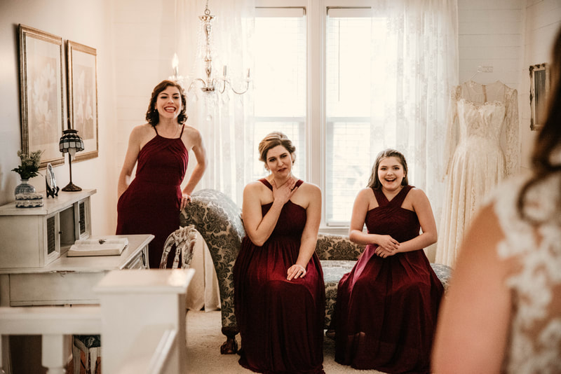 bridesmaids in cabernet colored dresses react to bride's dress