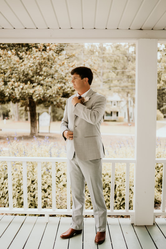 groom in gray suit posing on farmhouse front porch