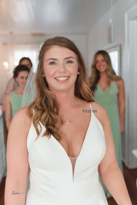 bride in farmhouse bridal suite with bridesmaids in sage dresses standing behind her