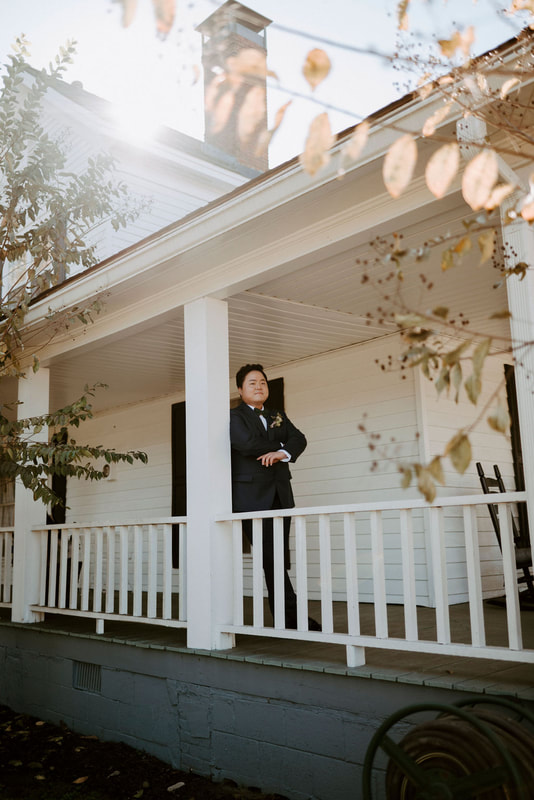 groom posing on farmhouse front porch