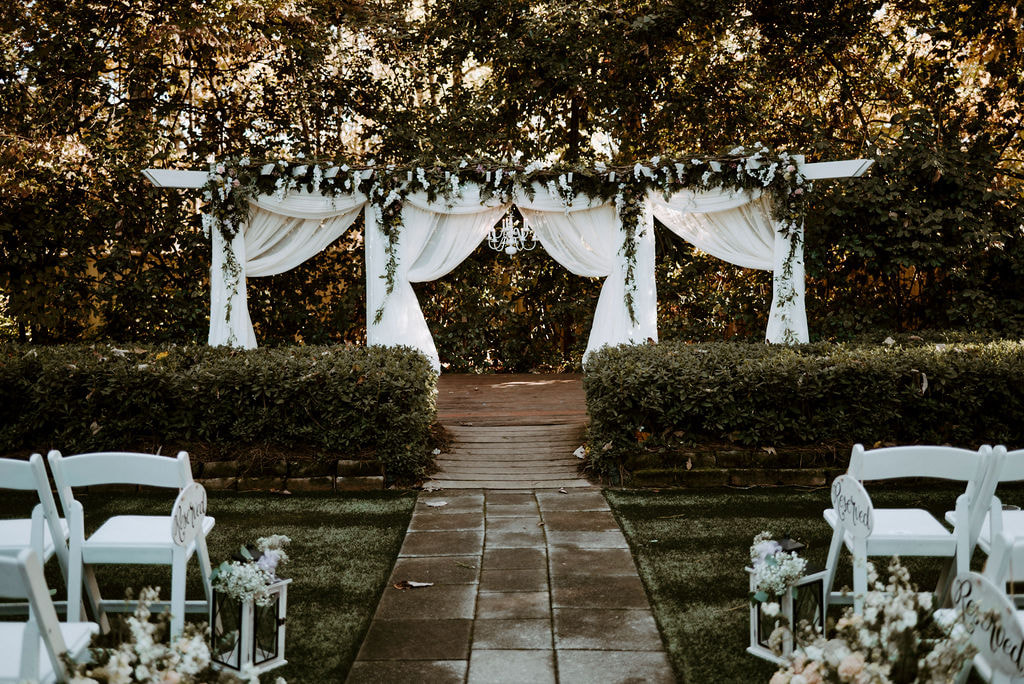 garden ceremony with lantern pew markers and dramatic arbor with theater curtains and greenery