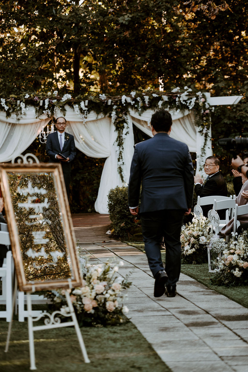 groom walking to garden ceremony altar with theater curtains and dramatic greenery
