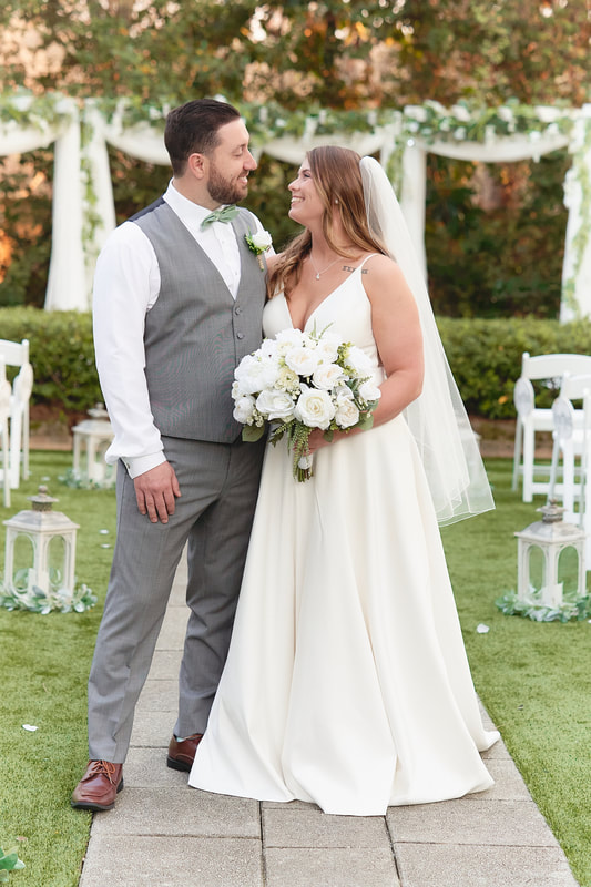 groom in gray pants and vest with sage green bow tie standing with bride in ceremony aisle