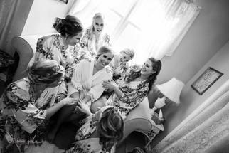 Bride sitting in the Bridal suite with her bridesmaids in a circle around her all smiling in robes