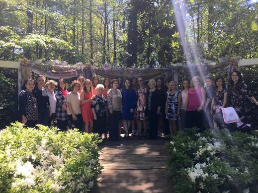 Picture of all the guests for Rebecca's bridal shower. All the girls are lined up by the outdoor arbor, which is decorated with burlap and purple flowers.