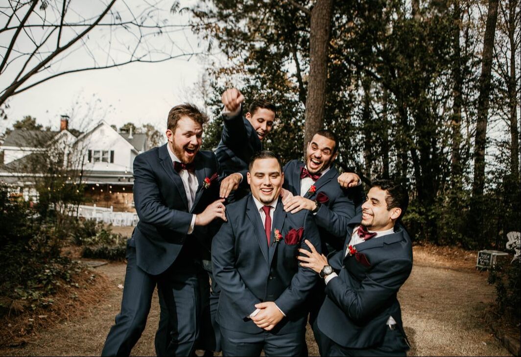 groomsmen in charcoal suits with burgundy details jumping on groom in matching suit