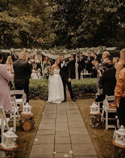 Picture of Jessica and Ryan at greenery-covered altar with a simply decorated aisle with white lanterns on wooden stumps.