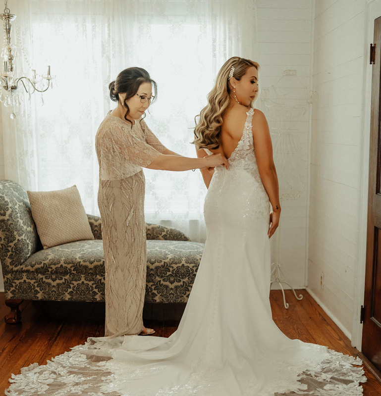 Mother of the bride assisting the bride with bridal gown