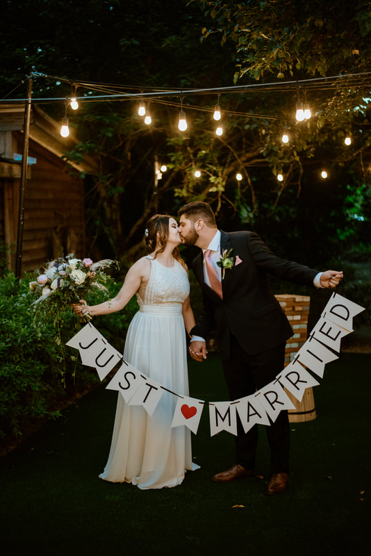 newlyweds kissing by rustic bar holding 'just married' sign