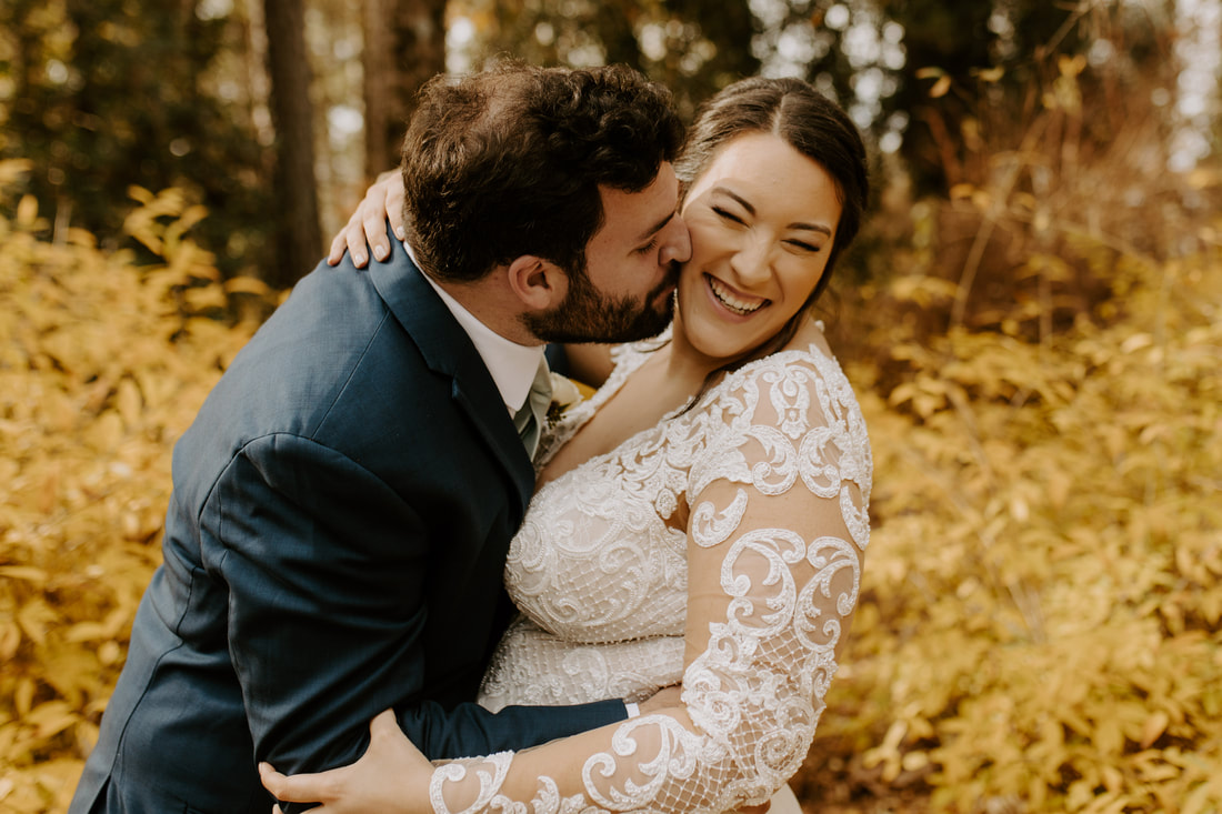groom kisses bride's cheek surrounded by gold bushes