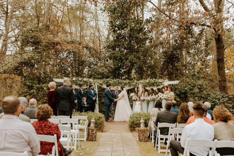 outdoor winter ceremony with altar decorated with greenery and aisle lined with lanterns on stumps