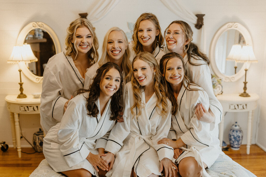 bride and bridesmaids in matching white robes sitting on farmhouse bed