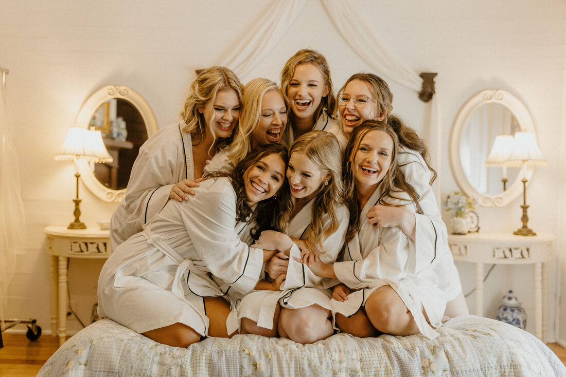 bride and bridal party laughing on bridal suite bed