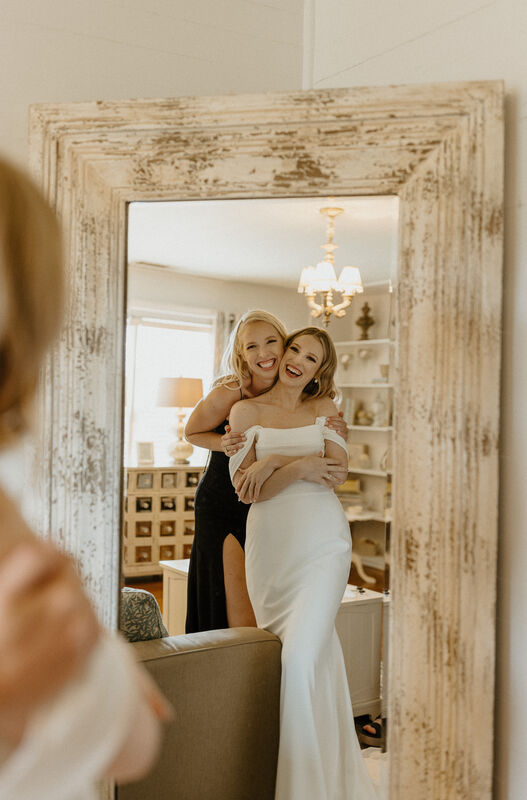 bride posing with sister in farmhouse bridal suite mirror