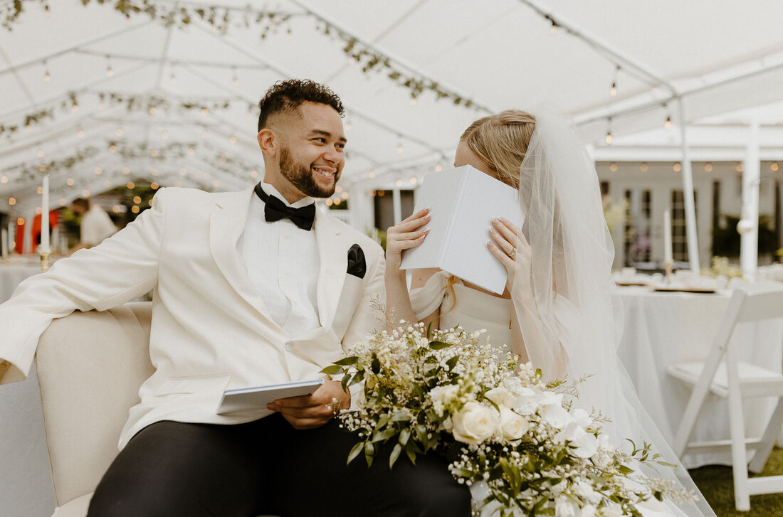 bride and groom in loveseat under reception tents reading vows