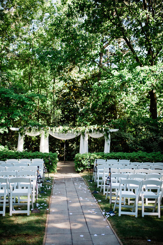 outdoor wedding altar covered in greenery, white flowers, and white chiffon