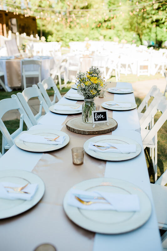 table with champagne runners, wood slices, chalkboard table numbers, and white and yellow bouquets
