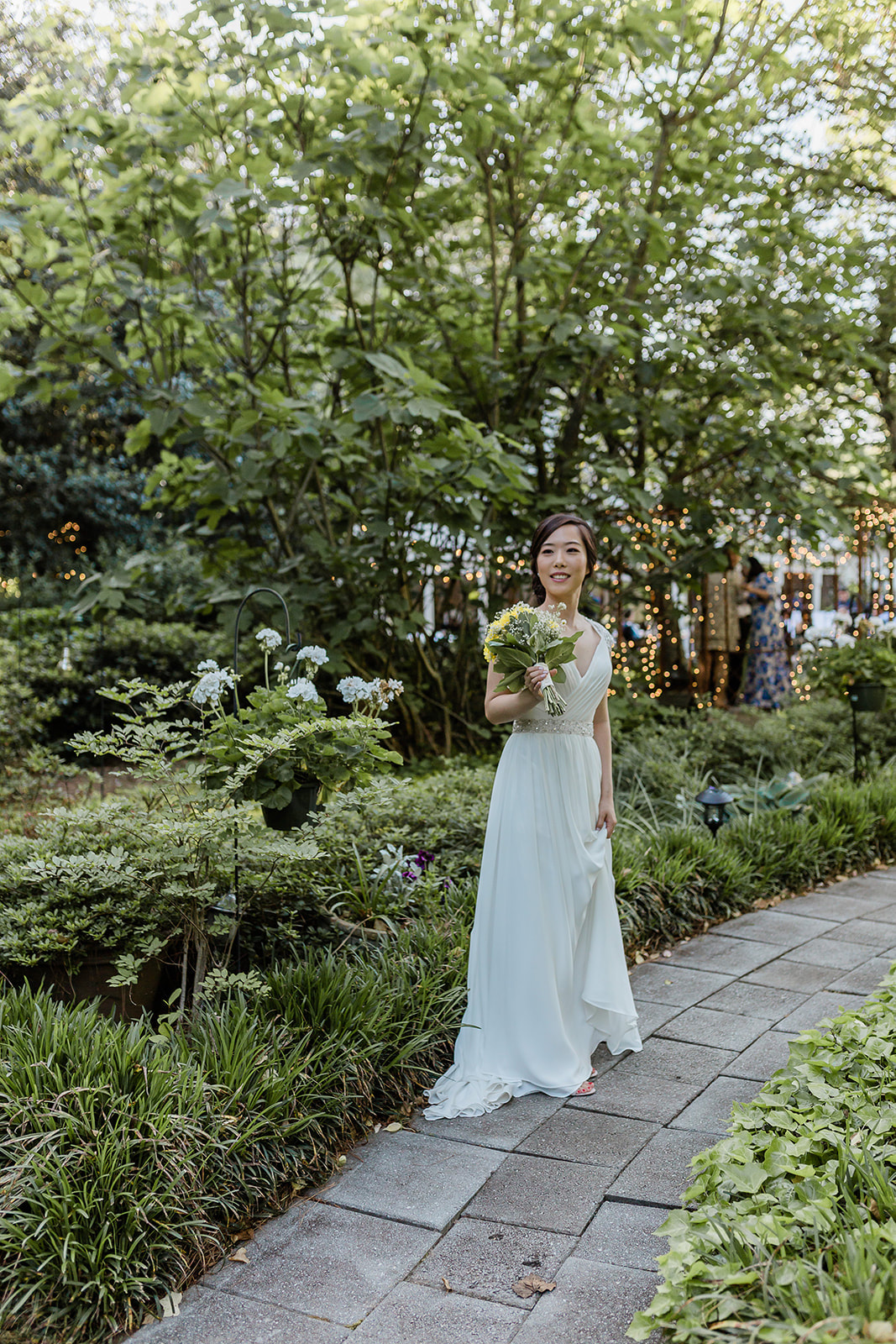 bride standing along garden path with potted plants and lush greenery