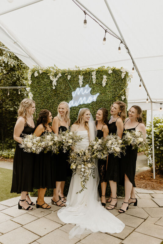bridal party in front of greenery wall with neon sign