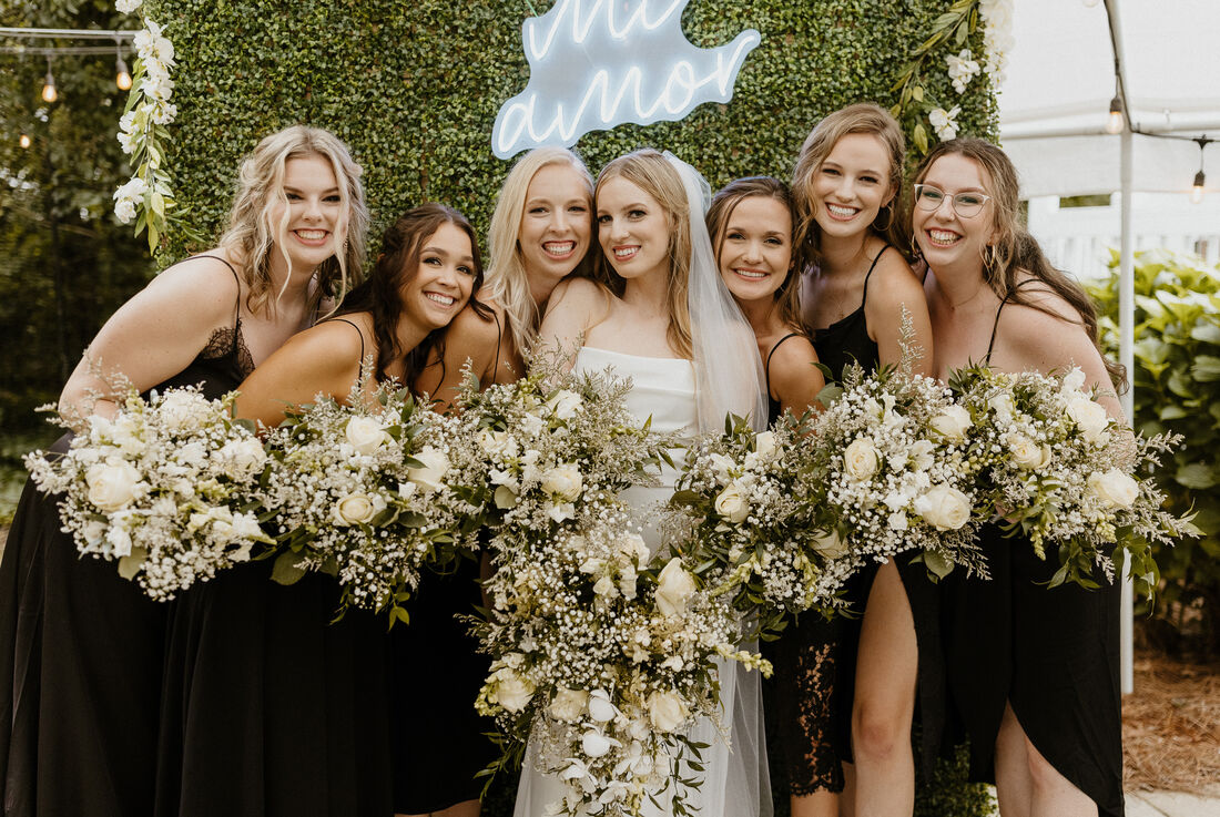 bride posing with bridesmaids all holding white bouquets with baby's breath and greenery