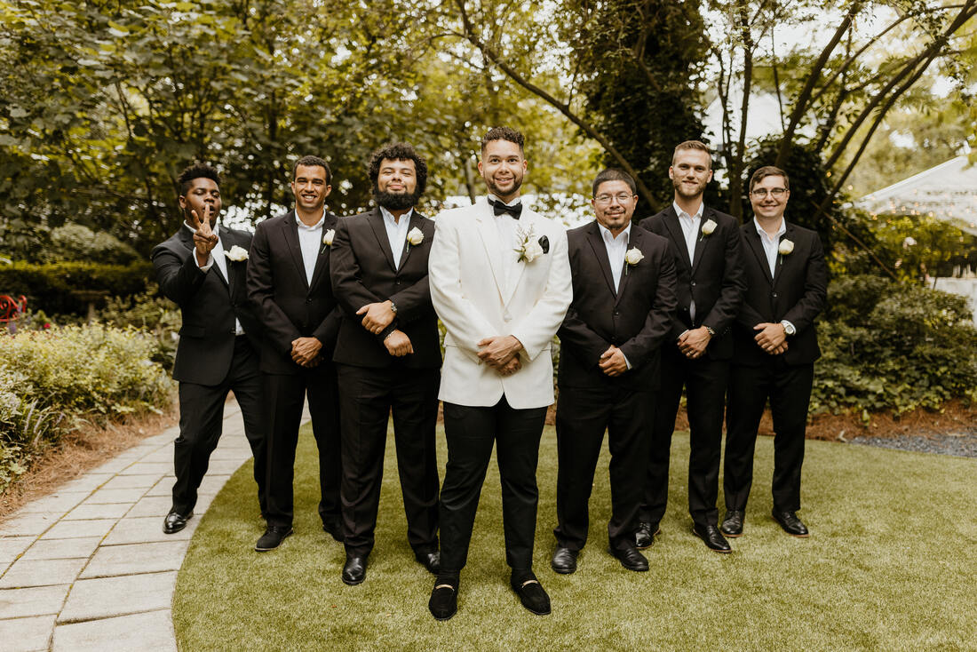 groom in white sports coat posing with groomsmen in all black