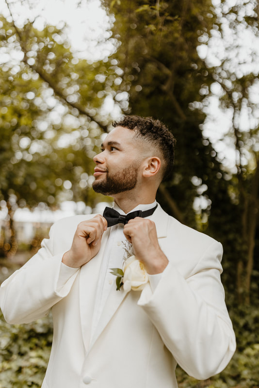 groom in white suit with black bow tie