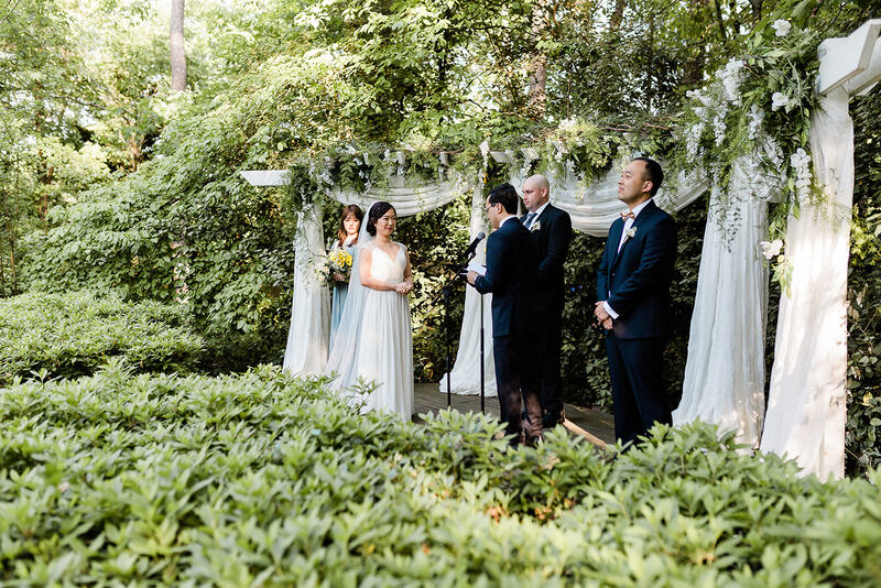 groom reading vows to bride at wedding alter surrounded by lush greenery