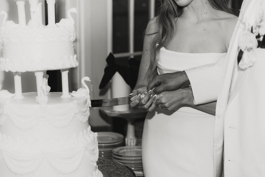 black and white photo of newlyweds using engraved cake cutting utensils with names and dates