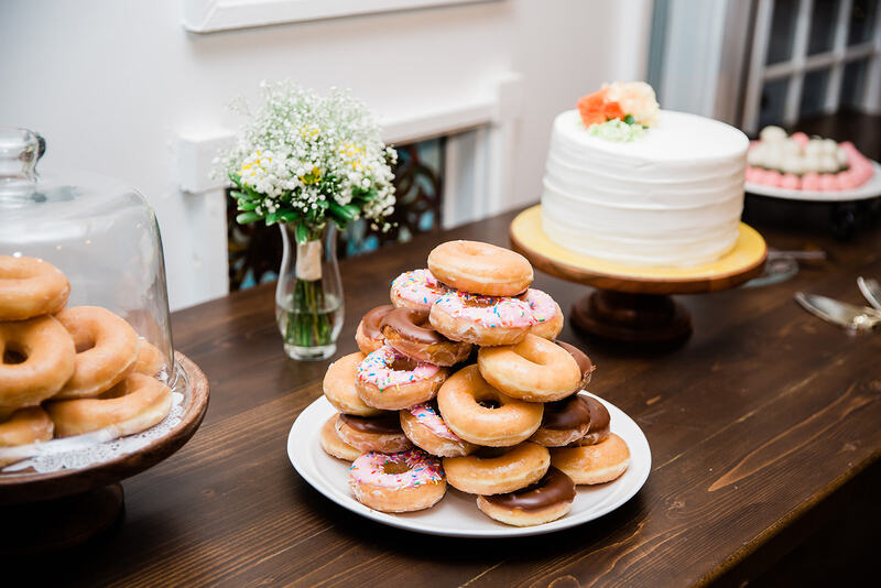 Donuts stacked on wood farm table by cake and truffles for wedding dessert