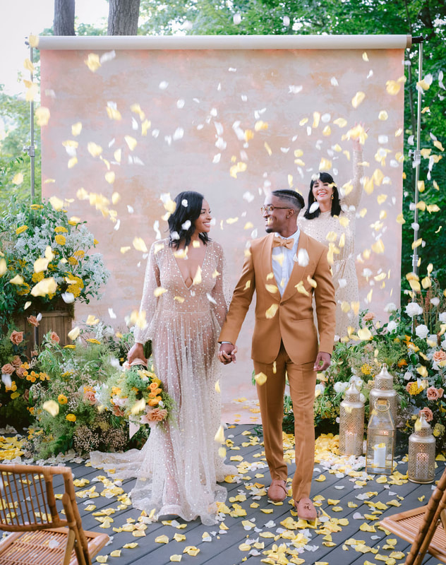 ceremony space decorated with floral arrangements and newlyweds walking down aisle with petals in air