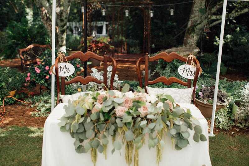 sweetheart table with greenery and mr and mrs chairs