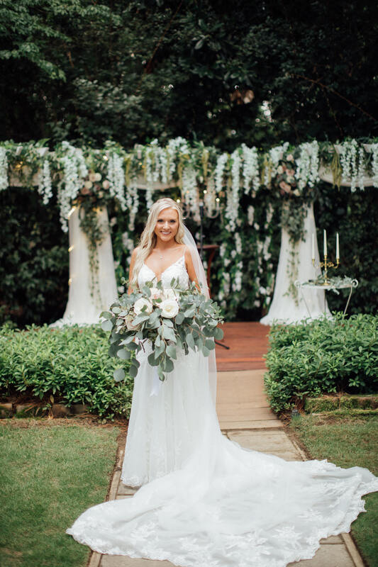 bride with large bouquet of eucalyptus and roses posing by arbor