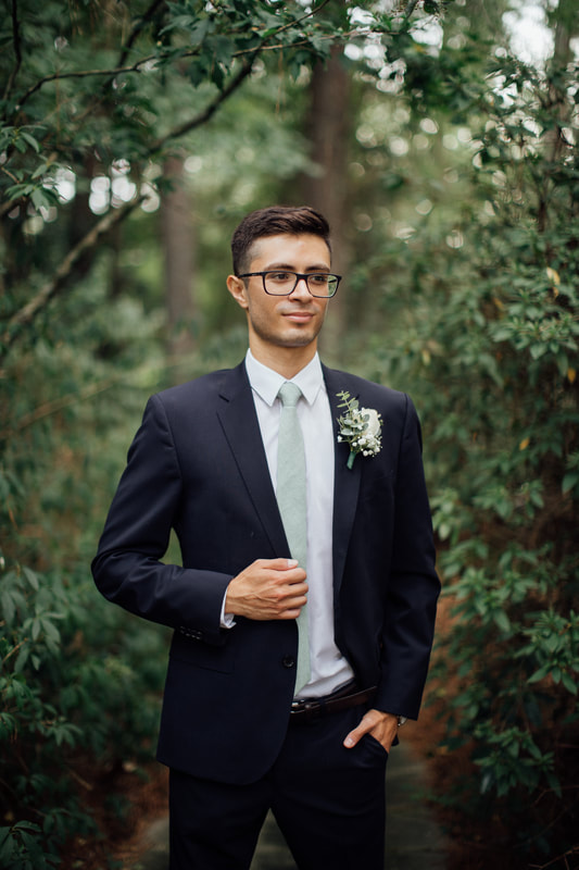 groom in dark suit with sage details standing in garden