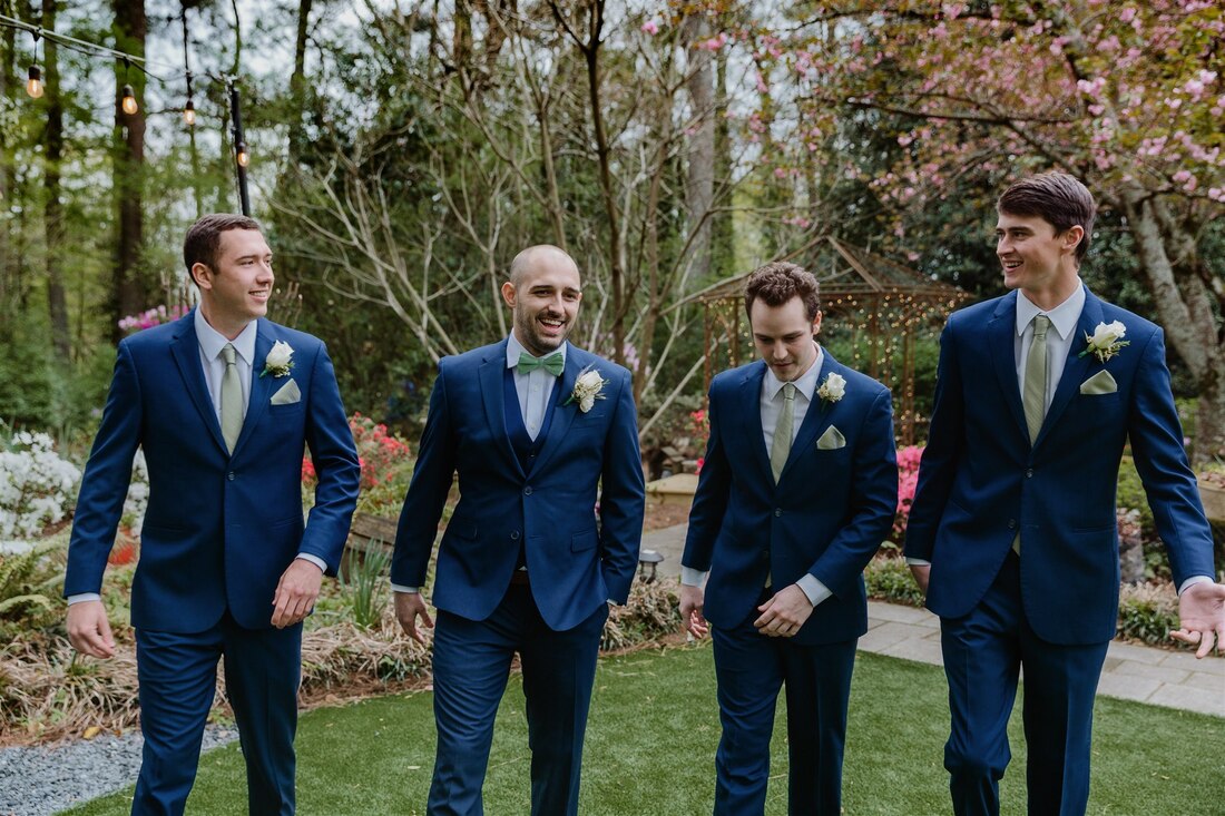 groom and groomsmen in navy suits with sage green ties and pocket squares