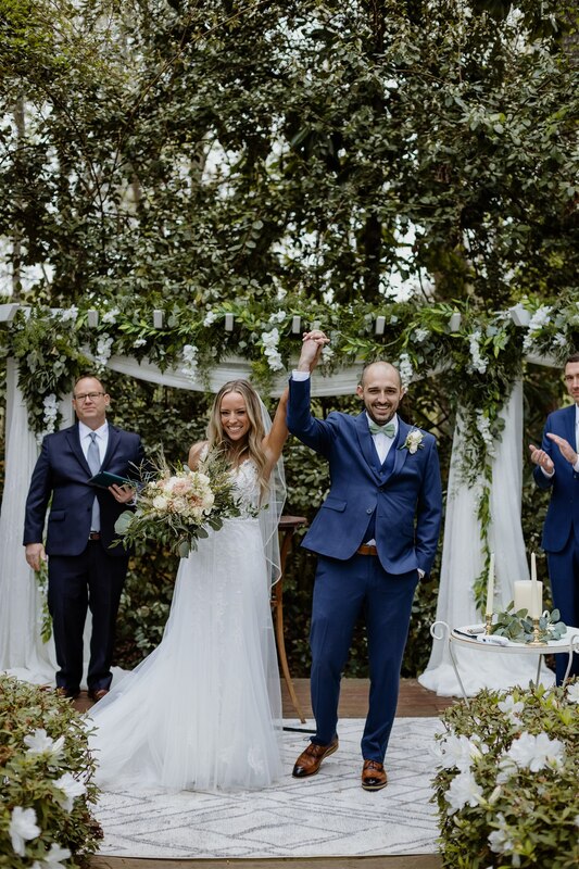 bride and groom holding hands up at altar with greenery
