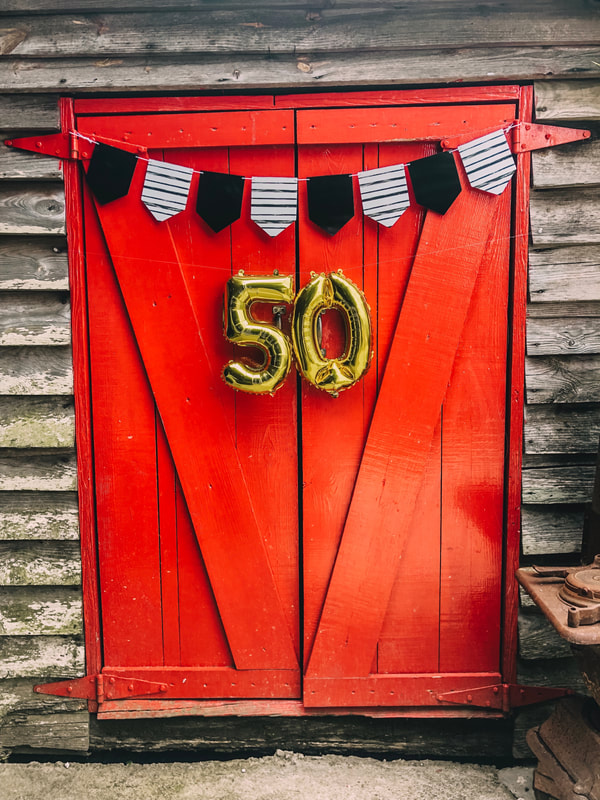 rustic red doors with gold '50' balloons, black and white banner for anniversary party