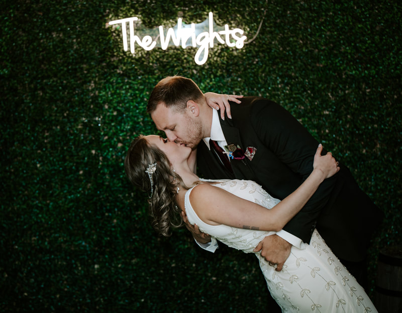 groom dips bride for kiss in front of neon sign with last name